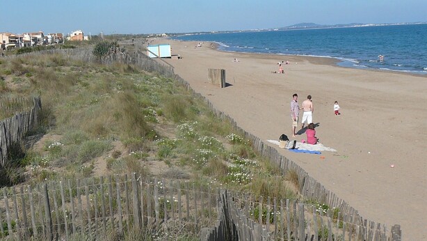 A beach with a wooden fence, a few people, and a small building in the background.