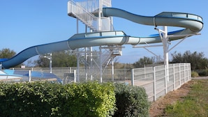 A water park with a large water slide structure, a fenced area, and a clear sky.