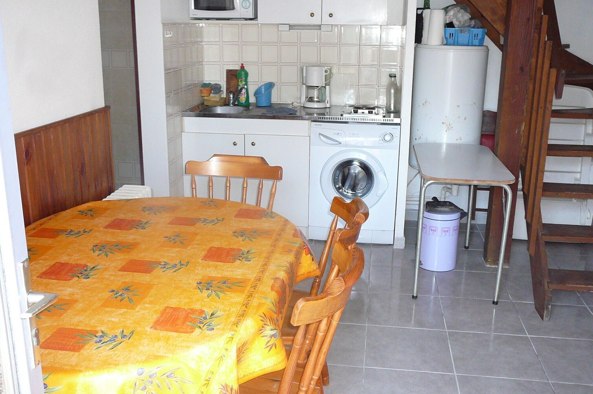A compact kitchen with a washing machine, a microwave, and a sink. There is a dining table with chairs and a small stool.