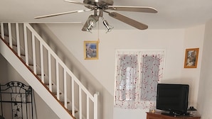 A living room with a staircase, a ceiling fan, a television on a wooden cabinet, and a brown sofa.