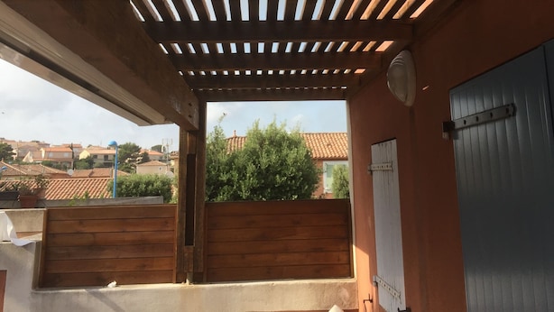 A balcony with a wooden pergola, a view of the neighborhood, and a blue door.