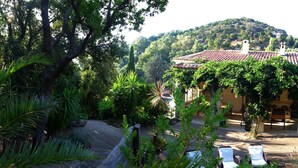 Eine Villa mit Ziegeldach, umgeben von üppiger Vegetation und einer Hügelkulisse im Hintergrund.