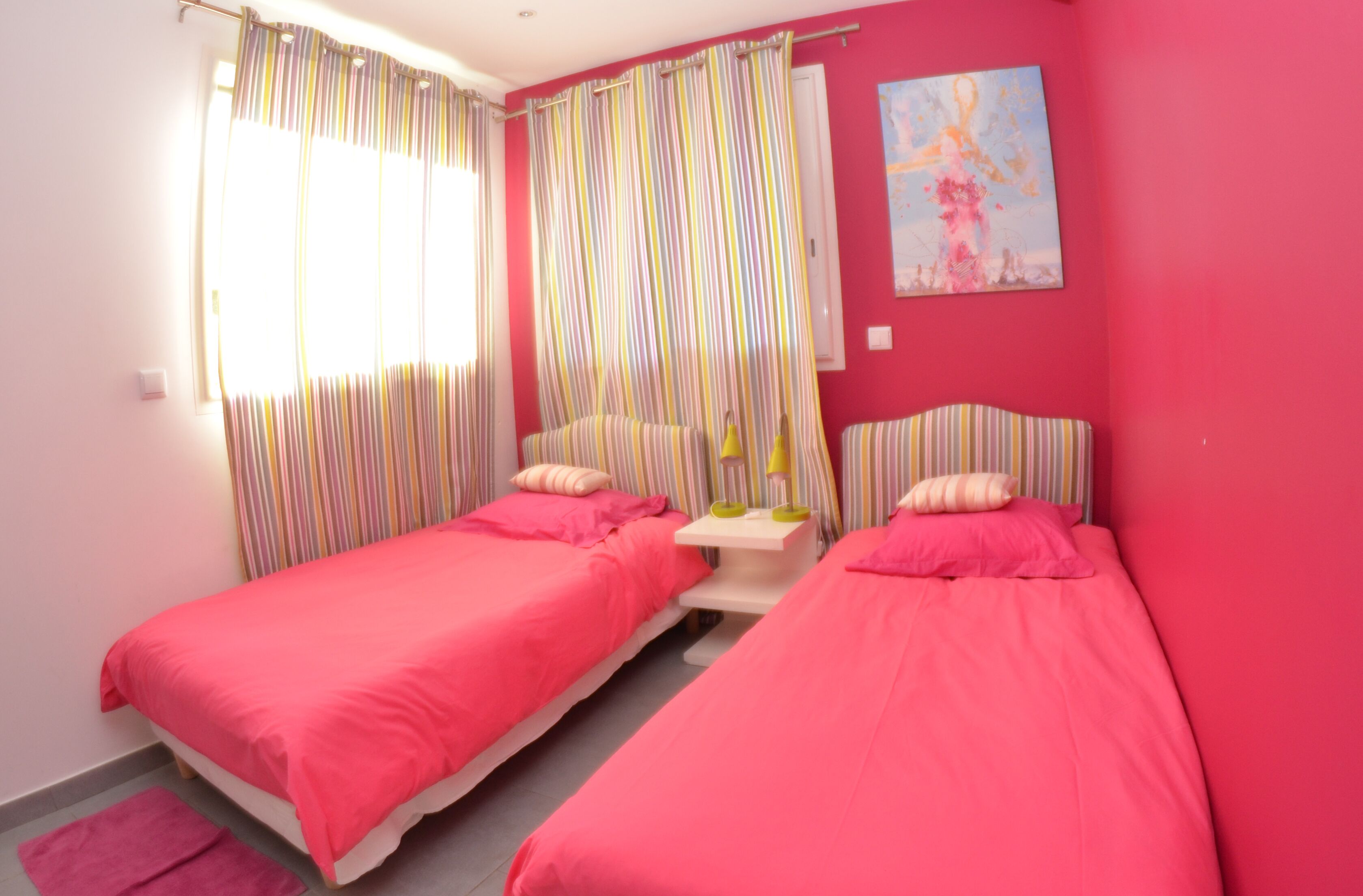 Une chambre avec deux lits, une petite table et un tableau au mur.