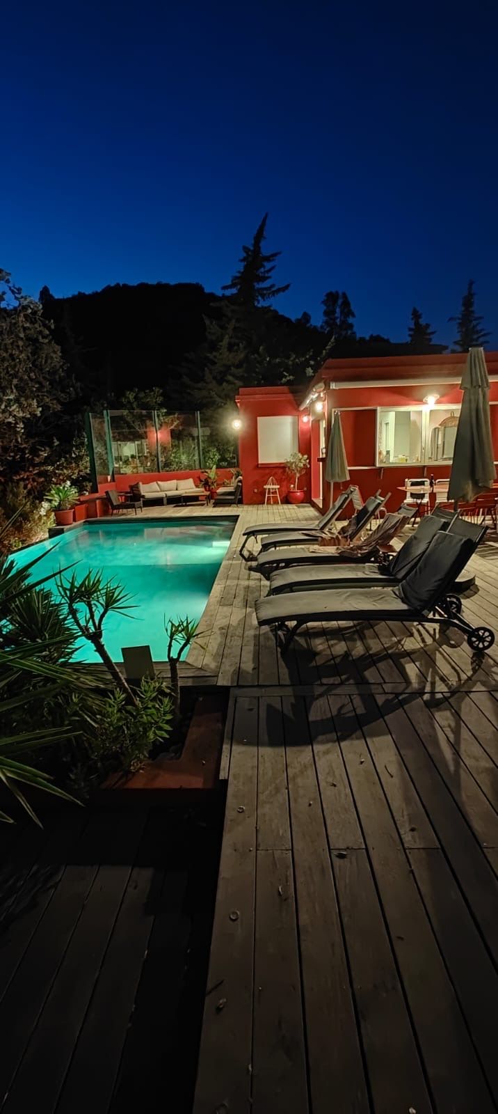 Terraza de madera con sillones de descanso y una piscina al anochecer.