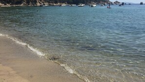 Ein Strand mit klarem Wasser, sandigem Ufer und Booten in der Ferne.