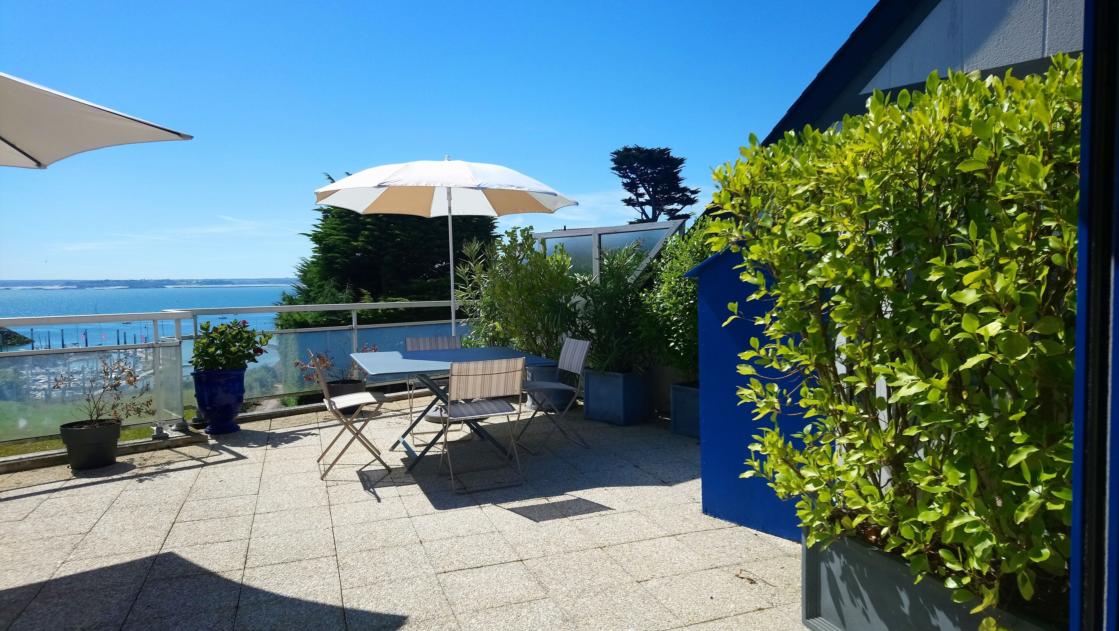 Une terrasse avec une table et des chaises, un grand parasol et une vue sur la mer.