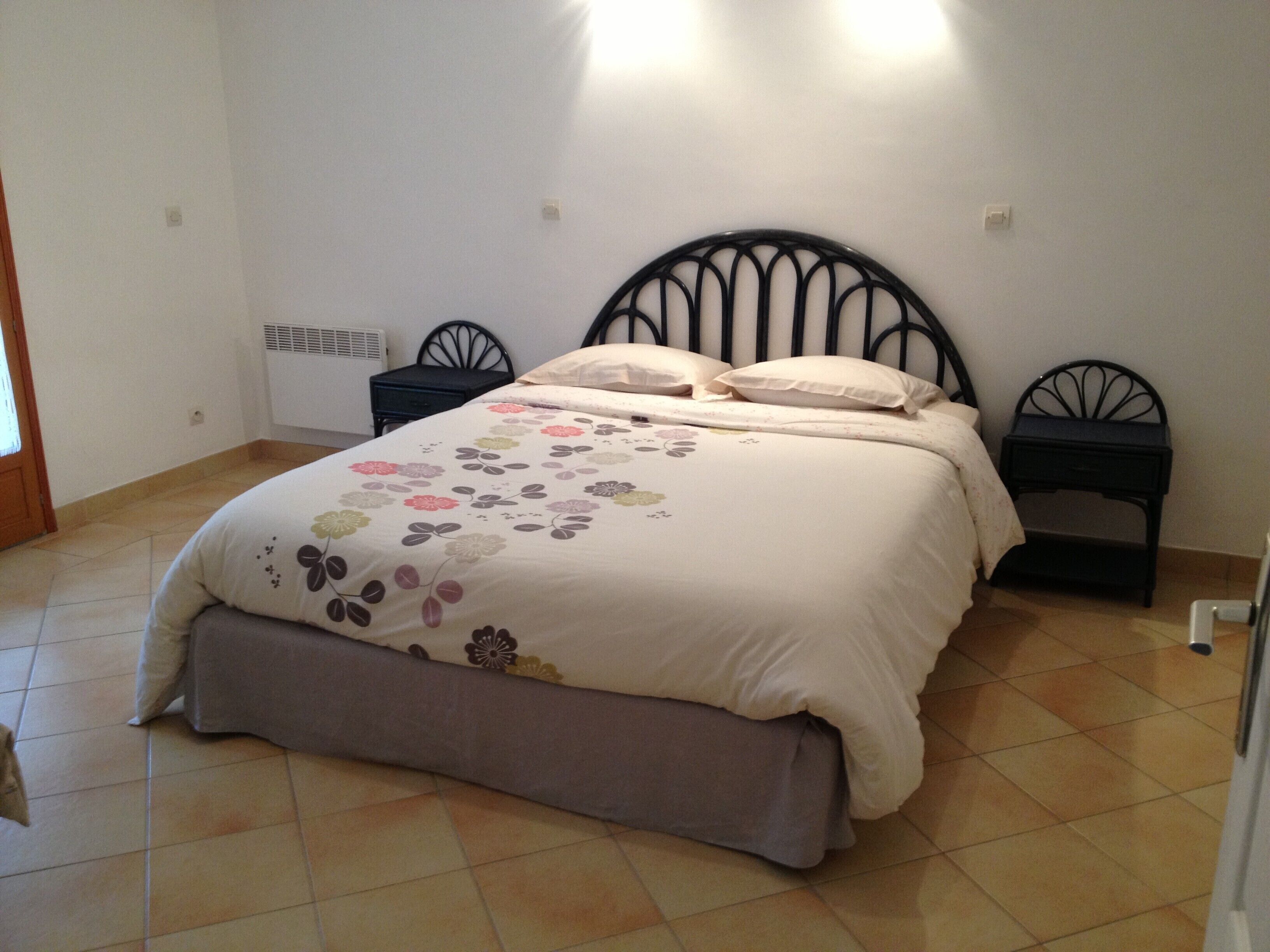 A bedroom with a bed, two bedside tables, a radiator, and a door.