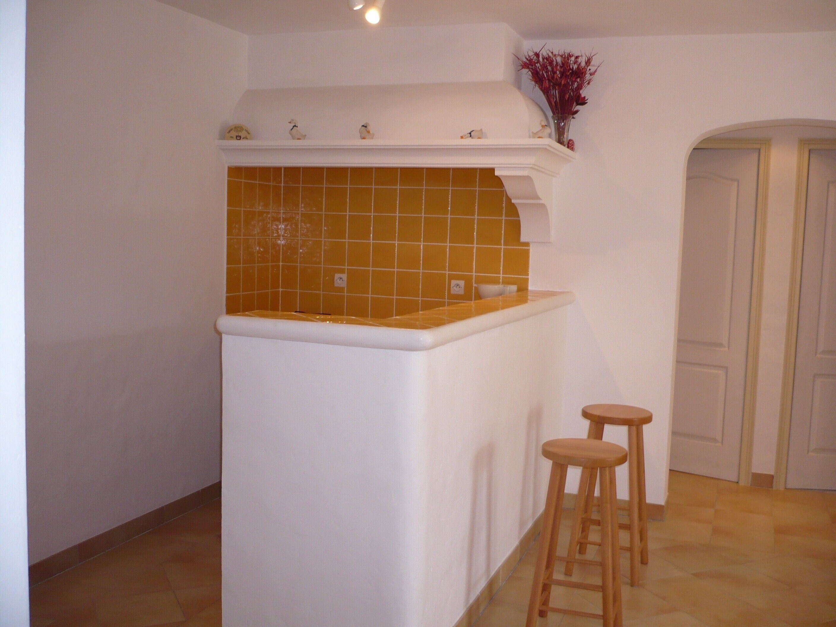 A kitchen with a white countertop, a yellow-tiled backsplash, and two wooden stools.