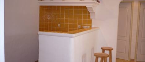 A kitchen with a white countertop, a yellow-tiled backsplash, and two wooden stools.