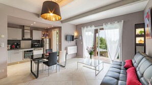 Un salon moderne avec un canapé en cuir noir, une table à manger avec des chaises, un coin cuisine équipé d’un four à micro-ondes et une grande fenêtre avec des rideaux.