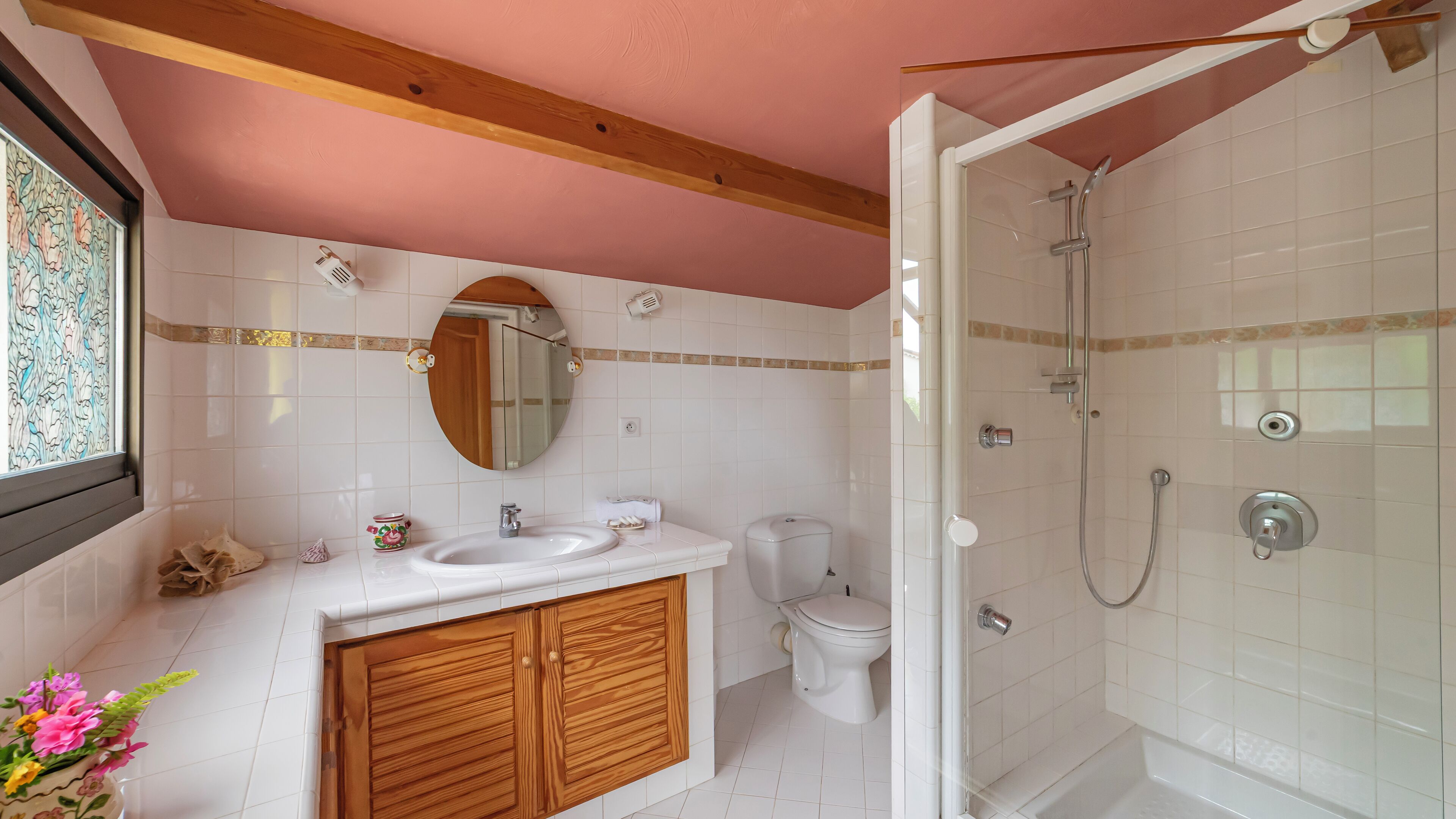 Un baño con lavamanos blanco, tocador de madera, inodoro y ducha con mampara de vidrio.