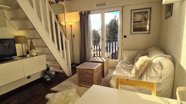 A cozy living room with a staircase, a sofa, a small table, and a television.