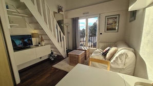 A living room with a white sofa, a TV, a staircase, and a balcony with a view.