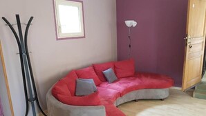 A room with a curved grey sofa, a standing lamp, and a door. - APARTMENT / VACATION RENTAL: 3 BEDROOMS, FOR 1 TO 6 PEOPLE (Vayrac)