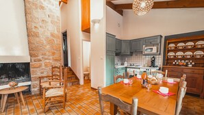 Un'accogliente zona pranzo con tavolo e sedie in legno, un muro in pietra e una cucina con mobili color petrolio e un forno a microonde.
