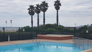 A rectangular swimming pool with a metal ladder, surrounded by a low fence and palm trees. - Apartment facing the SEA and BEACH with view of POND and MOUNTAIN (Canet-En-Roussillon)