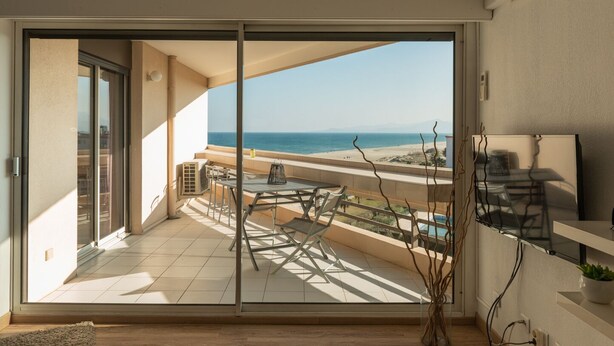 A balcony with a view of the sea, a table with chairs, and a TV on the wall. - Apartment facing the SEA and BEACH with view of POND and MOUNTAIN (Canet-En-Roussillon)