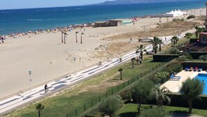 A beach with a paved walkway, palm trees, and a swimming pool. - Apartment facing the SEA and BEACH with view of POND and MOUNTAIN (Canet-En-Roussillon)
