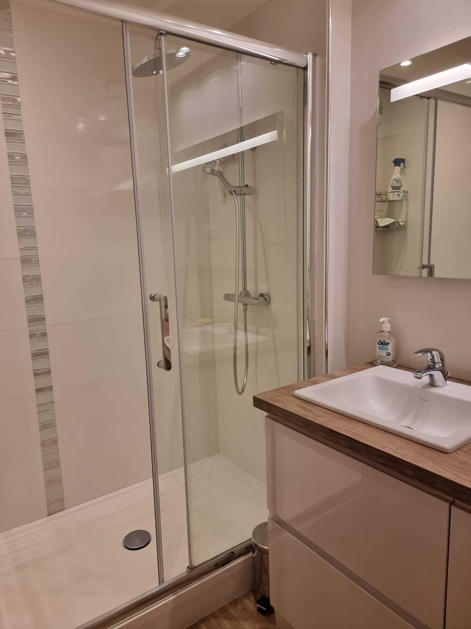 A modern bathroom with a glass-enclosed shower, a sink with a wooden countertop, and a mirror above the sink.