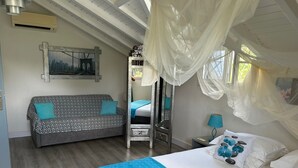 A bedroom with a bed, a sofa, a mirror, and a window with sheer curtains. - Villa Majeya - Modern comfort, exotic setting near the beach                    (SAINT-FRANCOIS)