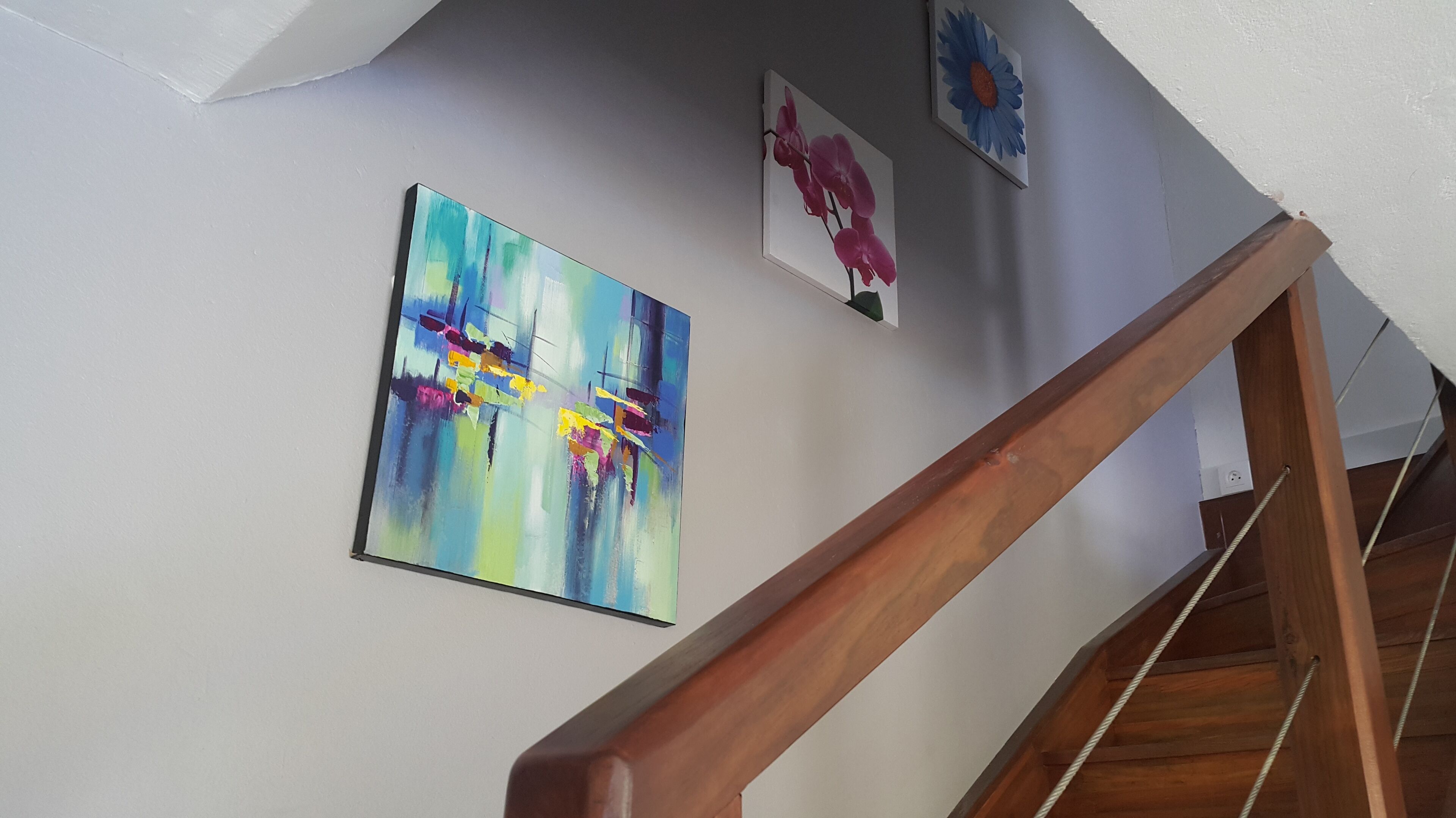 A staircase with wooden handrails and a white wall with three framed artworks.