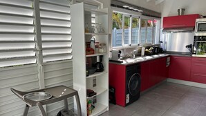 A modern kitchen with a built-in washing machine, a compact dining area with a cart, and a window with a view of greenery. - Villa Majeya - Modern comfort, exotic setting near the beach                    (SAINT-FRANCOIS)