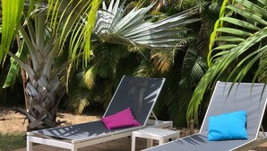 Two white sun loungers with black cushions and colorful pillows, placed on a wooden deck surrounded by tropical plants. - Villa Majeya - Modern comfort, exotic setting near the beach                    (SAINT-FRANCOIS)