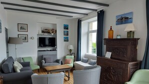 A living room with a TV, wooden flooring, and various seating options including a sofa, armchairs, and a coffee table. - Breton family house with magnificent sea views (Carantec)