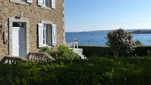 A stone building with a white door and shutters, a small porch with steps, and a view of the sea with boats. - Breton family house with magnificent sea views (Carantec)