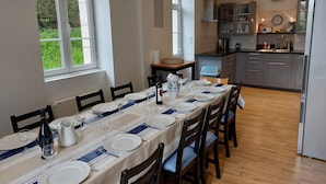 A dining area with a table set for four, a kitchen in the background, and a window with greenery outside. - Breton family house with magnificent sea views (Carantec)