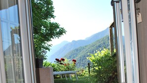 A doorway leading to a balcony with a view of mountains and a garden.