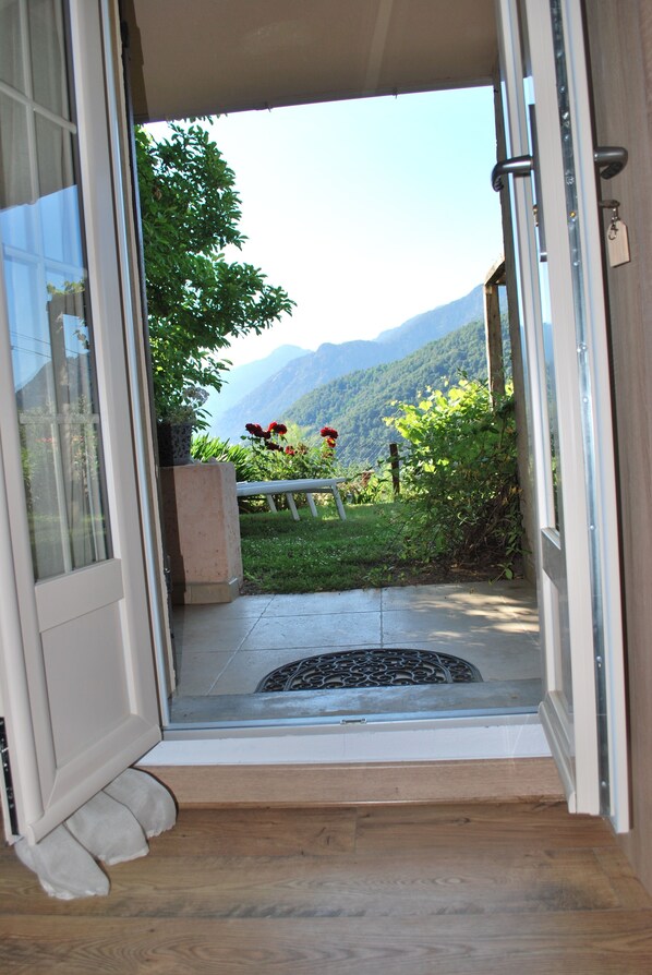 A doorway leading to a balcony with a view of mountains and a garden.