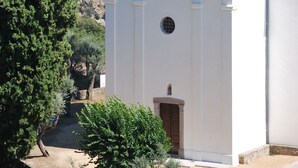 A white building with a red roof, surrounded by greenery and mountains.