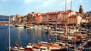 Un port de plaisance où sont amarrés de nombreux bateaux, une ville historique aux bâtiments aux toits rouges et un imposant beffroi.