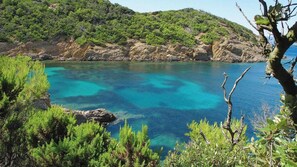 A coastal landscape with clear turquoise waters, rocky terrain, and dense green vegetation.