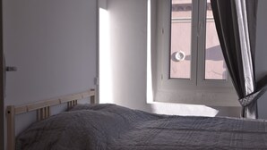 A bedroom with a bed, a window with curtains, and a view of the street outside. - 100m from the beach, apartment with river view, small garden for meals (Agde)
