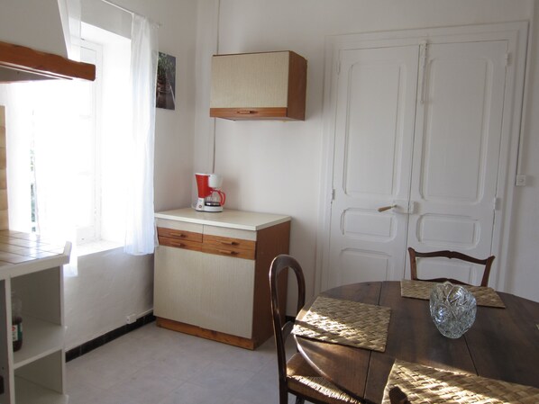 Une petite cuisine avec une machine à café sur le plan de travail, un meuble en bois et une table à manger avec des chaises.