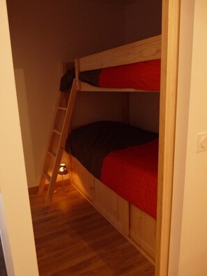 A bunk bed with a ladder, wooden flooring, and a red blanket.