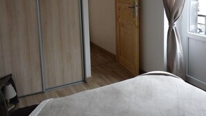 A bedroom with a bed, a wooden wardrobe, a door, and a window with curtains.