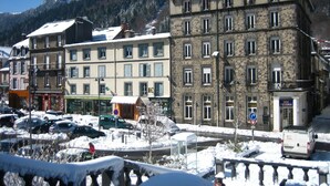 A snow-covered street with historic buildings, a parking area, and a mountain in the background.