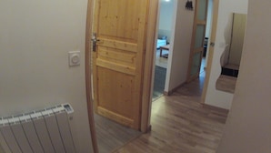 A hallway with a wooden door, a radiator, and a glimpse of a bedroom with a bed and a nightstand.