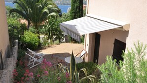 A patio with a table and chairs, surrounded by lush greenery and flowering plants. - Studio 2 persons propriano (Propriano)