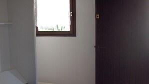 A single bed with a blue mattress in a room with white walls, a small window, and a dark door. - Studio 2 persons propriano (Propriano)