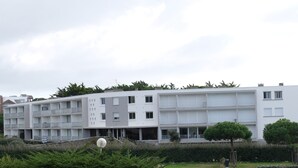 A modern multi-story residential building with balconies, a flat roof, and a well-maintained garden area. - Appt 55m², 4-5 pers, 100m beach, parking, adult bike hire, WIFI (Quiberon)