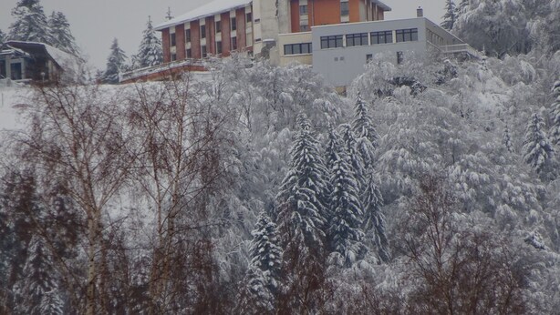 A building with a central tower and a flat-roofed section, surrounded by snow-covered trees. - Chalet''Le Chardon '' 67m2 + 20m2 rental from 2 to 7 people with modular option (La Bourboule)