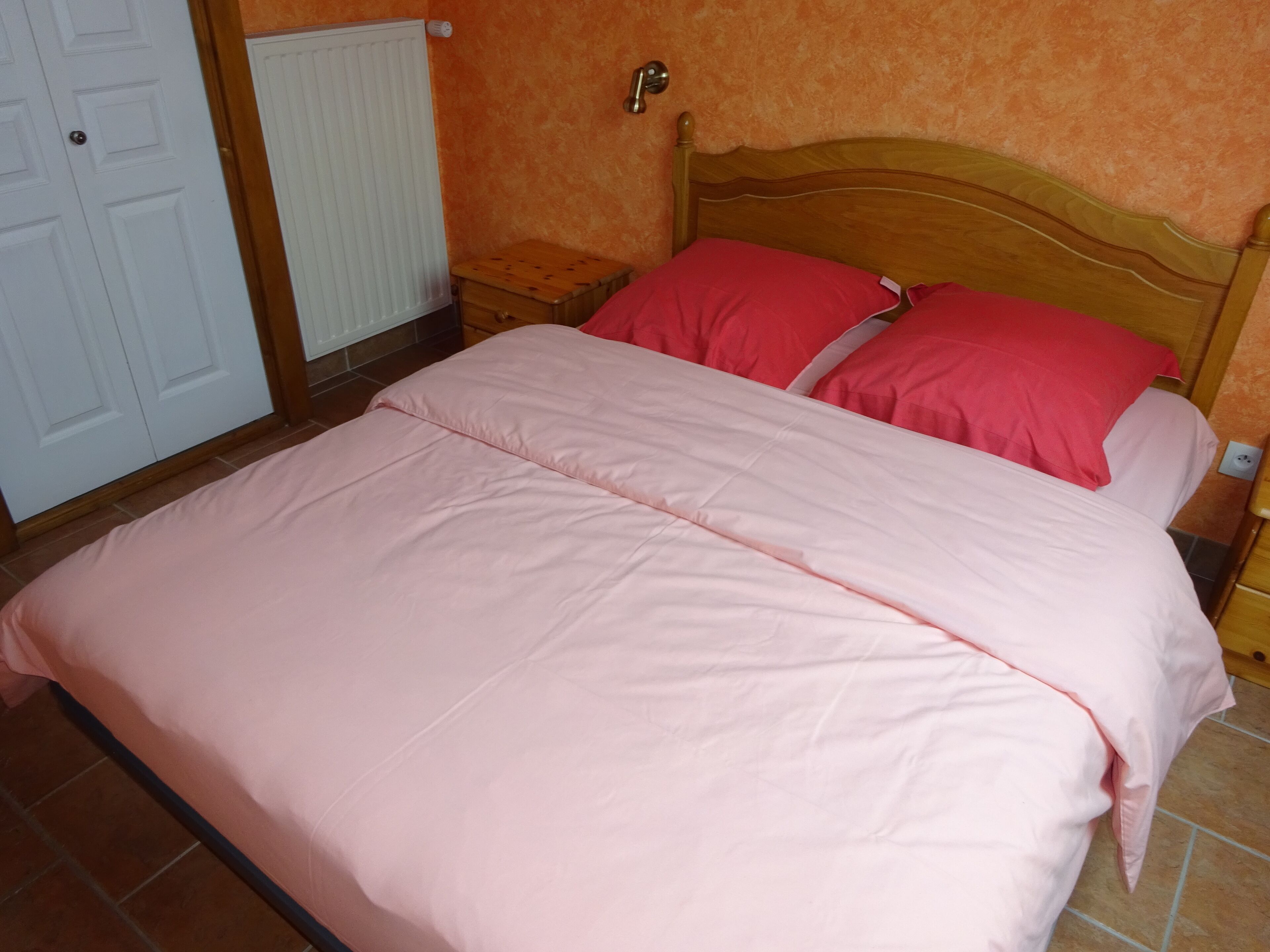 Une chambre à coucher avec un lit, une tête de lit en bois, une table de chevet, un radiateur blanc et une porte blanche.