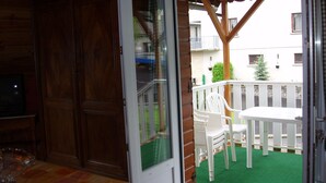 A room with a wooden door, a sliding glass door leading to an outdoor balcony with a white table and chairs, and a television on a stand. - Chalet''Le Chardon '' 67m2 + 20m2 rental from 2 to 7 people with modular option (La Bourboule)