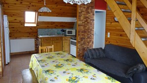 A cozy cabin interior with a dining table, sofa, kitchen area, and a wooden staircase. - Chalet''Le Chardon '' 67m2 + 20m2 rental from 2 to 7 people with modular option (La Bourboule)
