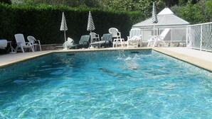 A swimming pool with clear water, surrounded by white lounge chairs and striped umbrellas.