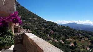 A hillside village with traditional stone buildings, a clear blue sky, and lush greenery.